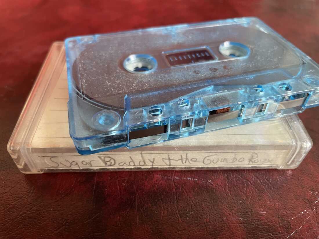 Une cassette se trouve sur le dessus de son boîtier, qui lit "Sugar Daddy & The Gumbo Roux".